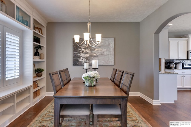 dining space with a chandelier, arched walkways, built in shelves, baseboards, and dark wood-style floors