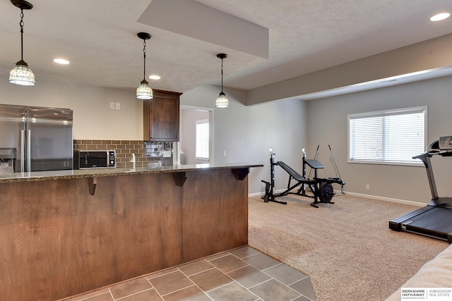 kitchen featuring stone counters, backsplash, carpet flooring, stainless steel fridge, and a kitchen breakfast bar