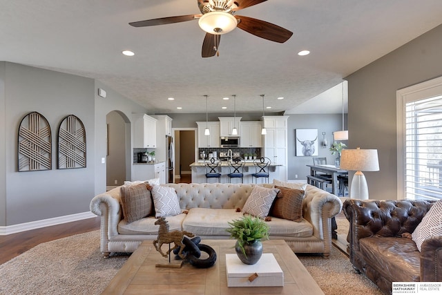 living area featuring arched walkways, light wood-style flooring, recessed lighting, a ceiling fan, and baseboards