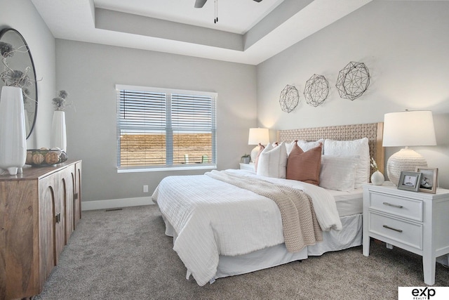 carpeted bedroom featuring a ceiling fan, a raised ceiling, and baseboards