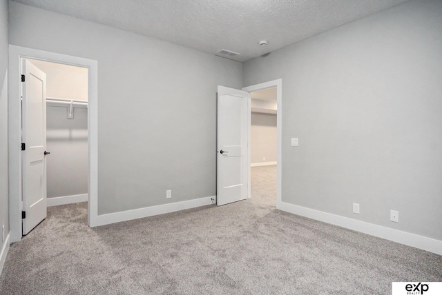 unfurnished bedroom with carpet, a spacious closet, visible vents, and baseboards