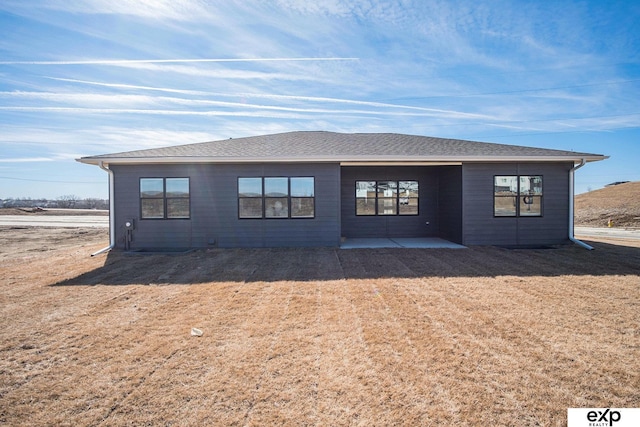 back of house with a patio, a shingled roof, and a lawn