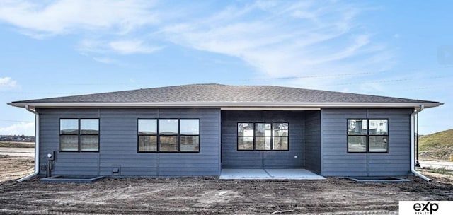 rear view of house featuring a patio and a shingled roof