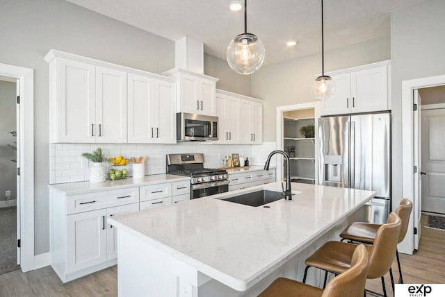 kitchen with stainless steel appliances, a sink, a center island with sink, and tasteful backsplash