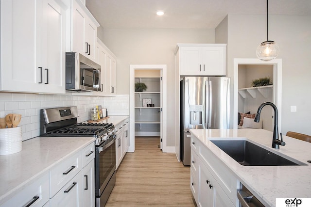 kitchen featuring light stone counters, appliances with stainless steel finishes, light wood-style floors, white cabinetry, and a sink