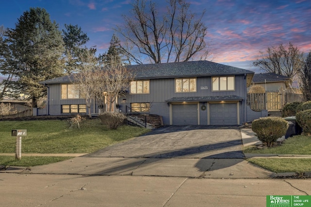 split foyer home featuring driveway, a garage, a shingled roof, fence, and a front yard