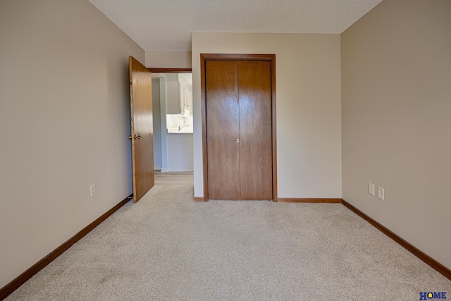 unfurnished bedroom with a textured ceiling, a closet, light carpet, and baseboards