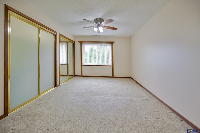 empty room with a textured ceiling, ceiling fan, baseboards, and light colored carpet