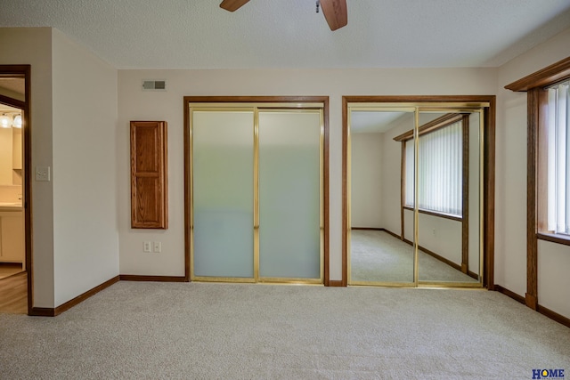 unfurnished bedroom featuring baseboards, visible vents, multiple closets, and light colored carpet