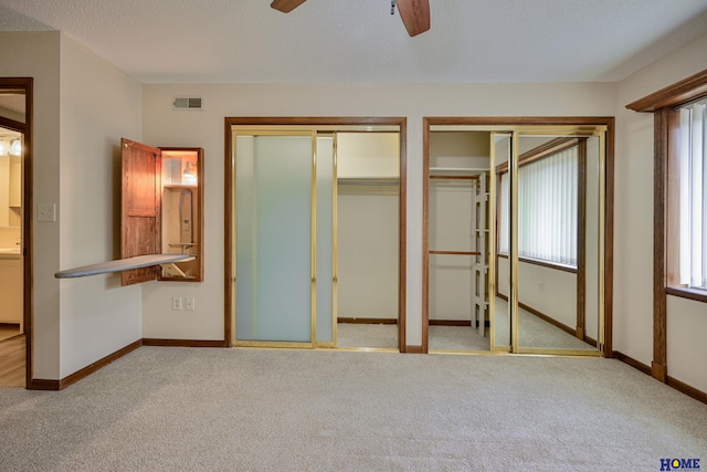 unfurnished bedroom with multiple closets, light colored carpet, visible vents, and baseboards