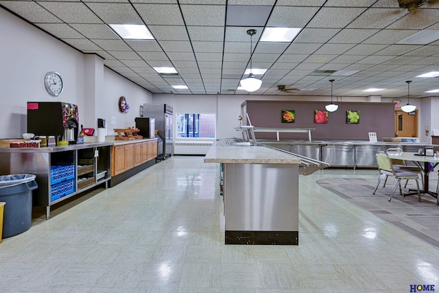 kitchen with a drop ceiling, open floor plan, light countertops, radiator, and pendant lighting