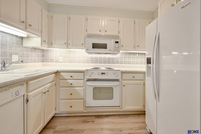 kitchen featuring white appliances, a sink, light countertops, backsplash, and light wood finished floors