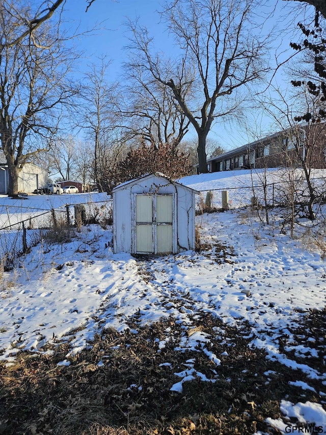 yard covered in snow featuring a storage shed, an outdoor structure, and fence