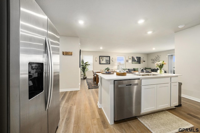 kitchen featuring light wood finished floors, white cabinets, appliances with stainless steel finishes, a kitchen island with sink, and light countertops