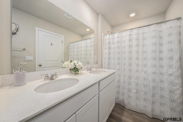 full bath featuring double vanity, visible vents, a sink, and wood finished floors