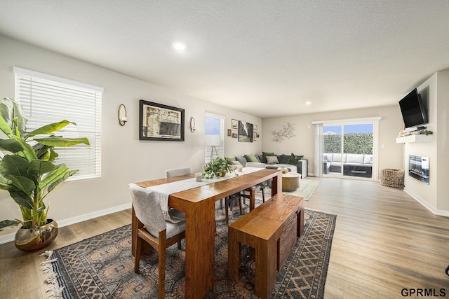 dining space featuring a glass covered fireplace, baseboards, light wood finished floors, and recessed lighting