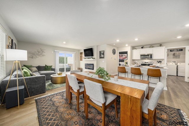 dining space featuring light wood-type flooring, a glass covered fireplace, washing machine and clothes dryer, and recessed lighting