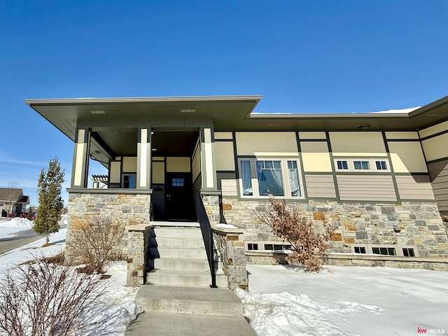 snow covered property entrance with stone siding