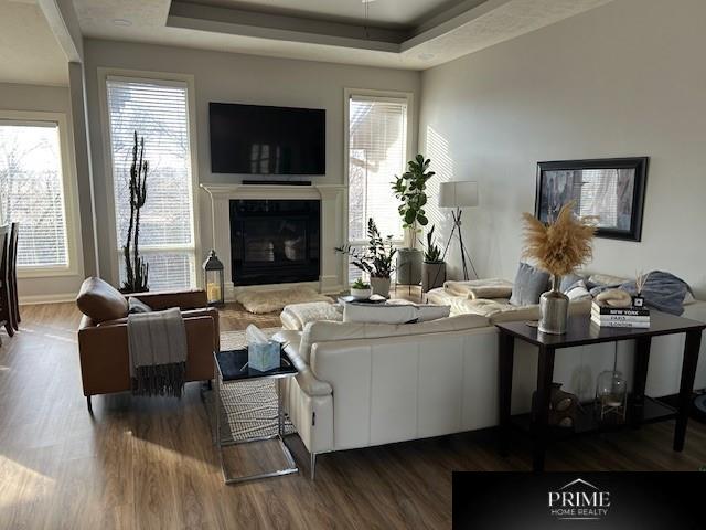 living area with dark wood-style floors, a tray ceiling, a glass covered fireplace, and baseboards