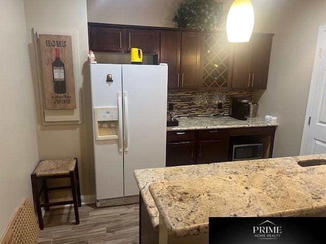 kitchen with light stone countertops, white fridge with ice dispenser, backsplash, and wood finished floors