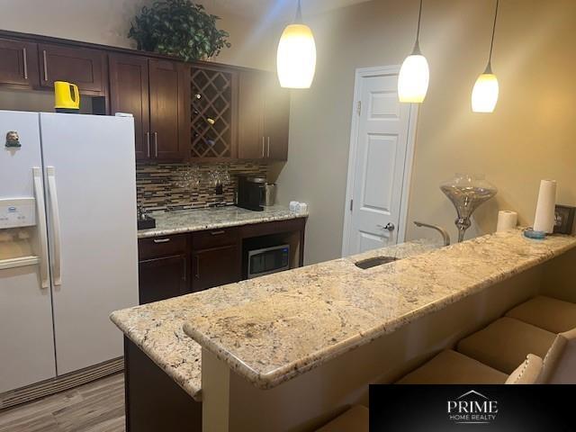 kitchen featuring pendant lighting, white fridge with ice dispenser, a sink, and a kitchen breakfast bar