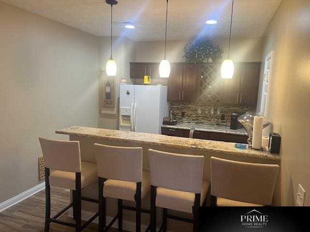 kitchen with hanging light fixtures, a kitchen bar, white refrigerator with ice dispenser, and light stone counters