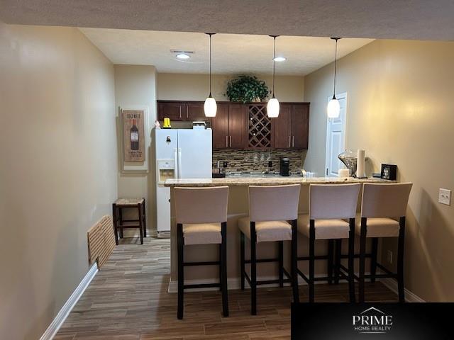 kitchen featuring visible vents, a kitchen breakfast bar, light countertops, backsplash, and pendant lighting