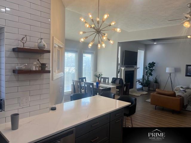 kitchen featuring open floor plan, dark cabinets, a fireplace, pendant lighting, and backsplash