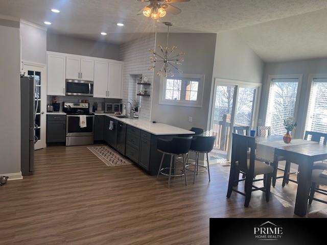 kitchen featuring dark wood-type flooring, decorative light fixtures, stainless steel appliances, light countertops, and white cabinetry