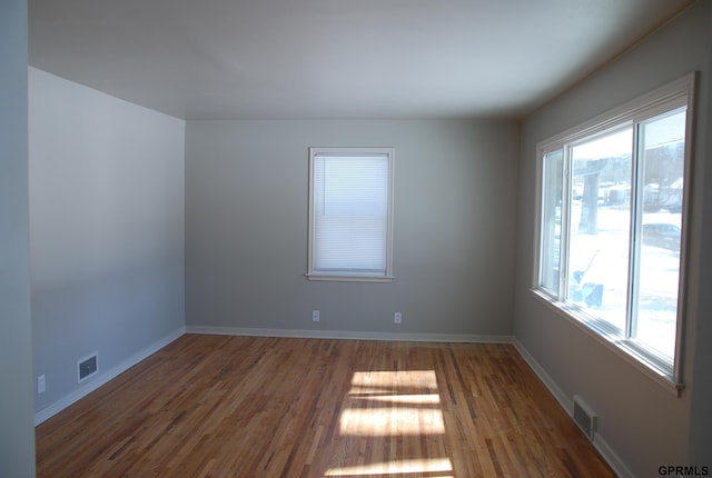 empty room with visible vents, dark wood-type flooring, and a wealth of natural light