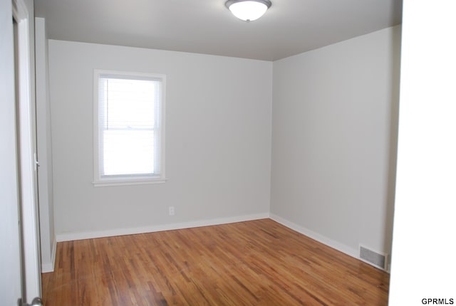 unfurnished room with wood finished floors, visible vents, and baseboards