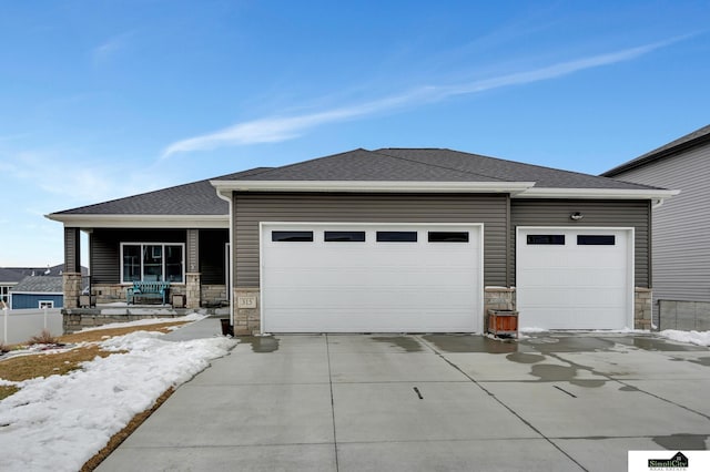 prairie-style home featuring concrete driveway, roof with shingles, covered porch, stone siding, and an attached garage