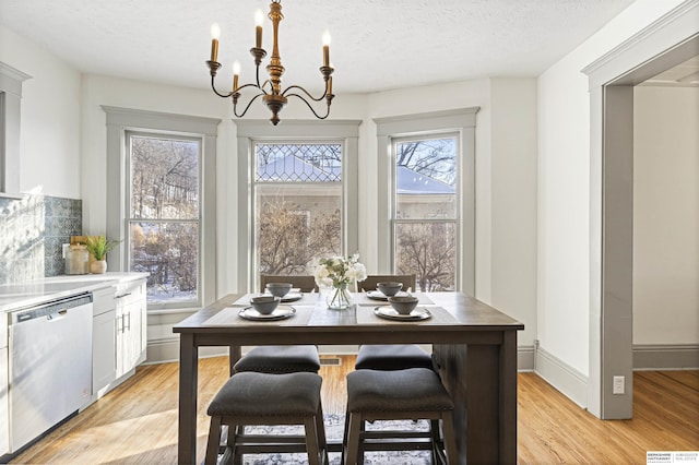 dining room featuring baseboards, a textured ceiling, light wood-style flooring, and an inviting chandelier