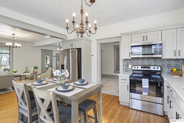 kitchen with appliances with stainless steel finishes, hanging light fixtures, light countertops, white cabinetry, and a notable chandelier