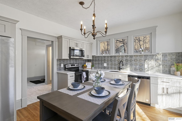 kitchen with decorative light fixtures, light countertops, light wood-style flooring, appliances with stainless steel finishes, and a sink