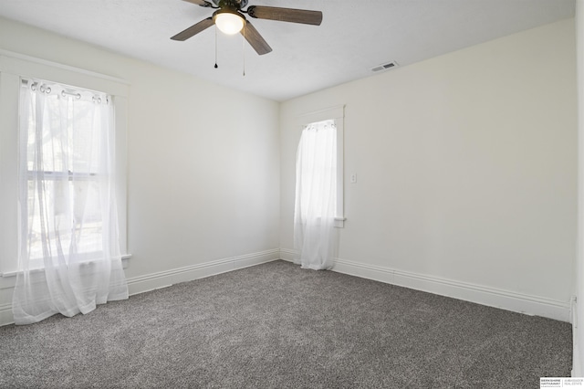 empty room featuring a ceiling fan, dark carpet, visible vents, and baseboards