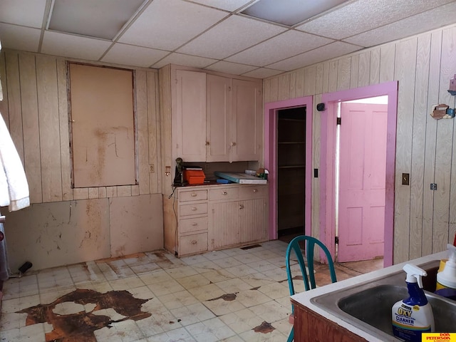 kitchen featuring light countertops, wood walls, a paneled ceiling, light floors, and a sink