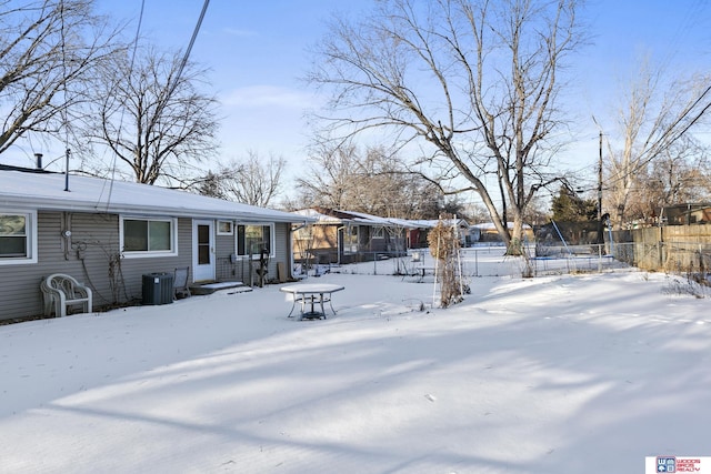 yard layered in snow with a trampoline, fence, and central AC