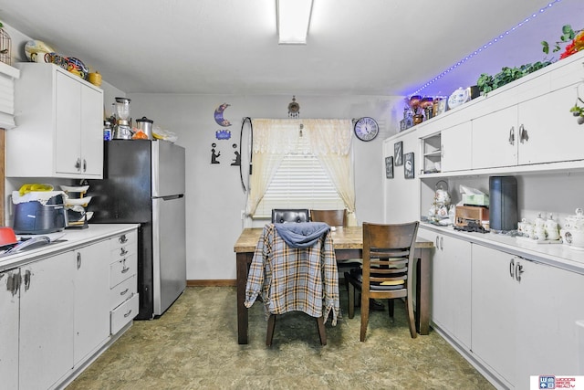 kitchen featuring light floors, white cabinets, light countertops, and freestanding refrigerator