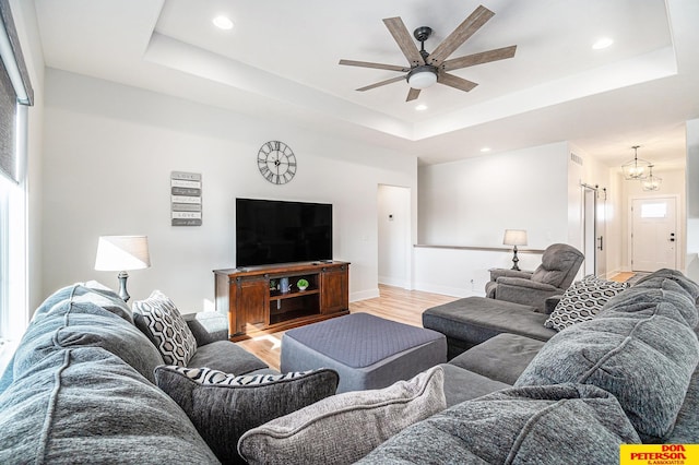 living room with light wood-type flooring, baseboards, and a tray ceiling