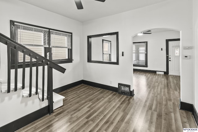 interior space featuring baseboards, arched walkways, a ceiling fan, and wood finished floors