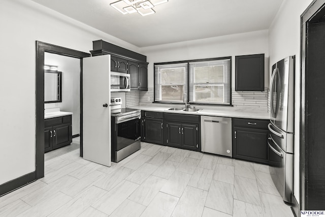 kitchen with decorative backsplash, appliances with stainless steel finishes, dark cabinets, light countertops, and a sink