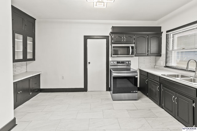 kitchen featuring tasteful backsplash, stainless steel appliances, dark cabinetry, light countertops, and a sink