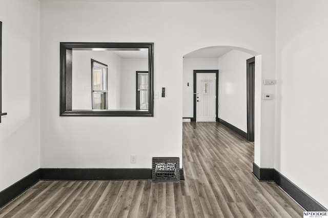 spare room with baseboards, arched walkways, and wood finished floors