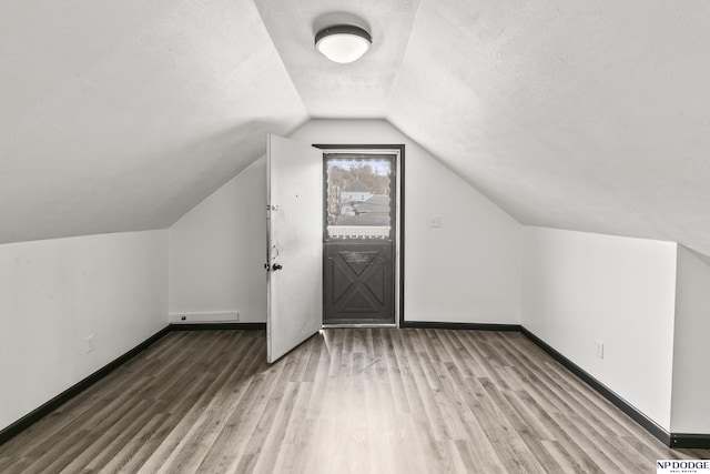 additional living space featuring lofted ceiling, a textured ceiling, baseboards, and wood finished floors