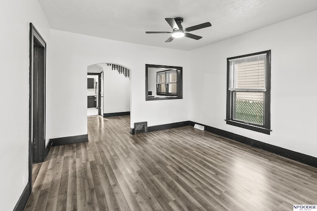 empty room featuring dark wood-style floors, baseboards, arched walkways, and ceiling fan