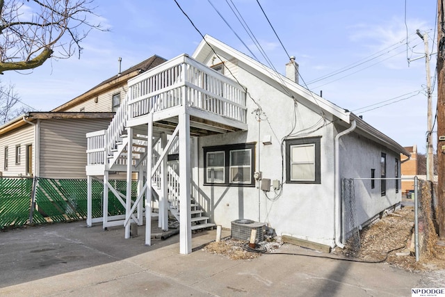 back of house featuring central AC unit, a chimney, stairway, fence, and stucco siding