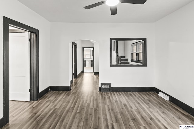 empty room with arched walkways, wood finished floors, and baseboards