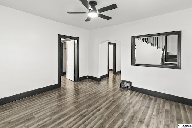 empty room featuring arched walkways, dark wood-style flooring, ceiling fan, and baseboards