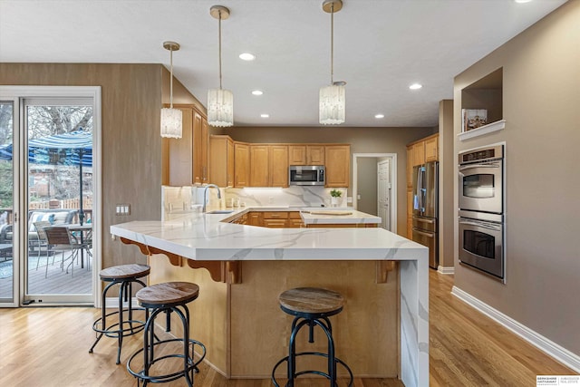 kitchen featuring a peninsula, appliances with stainless steel finishes, a sink, and light wood-style floors